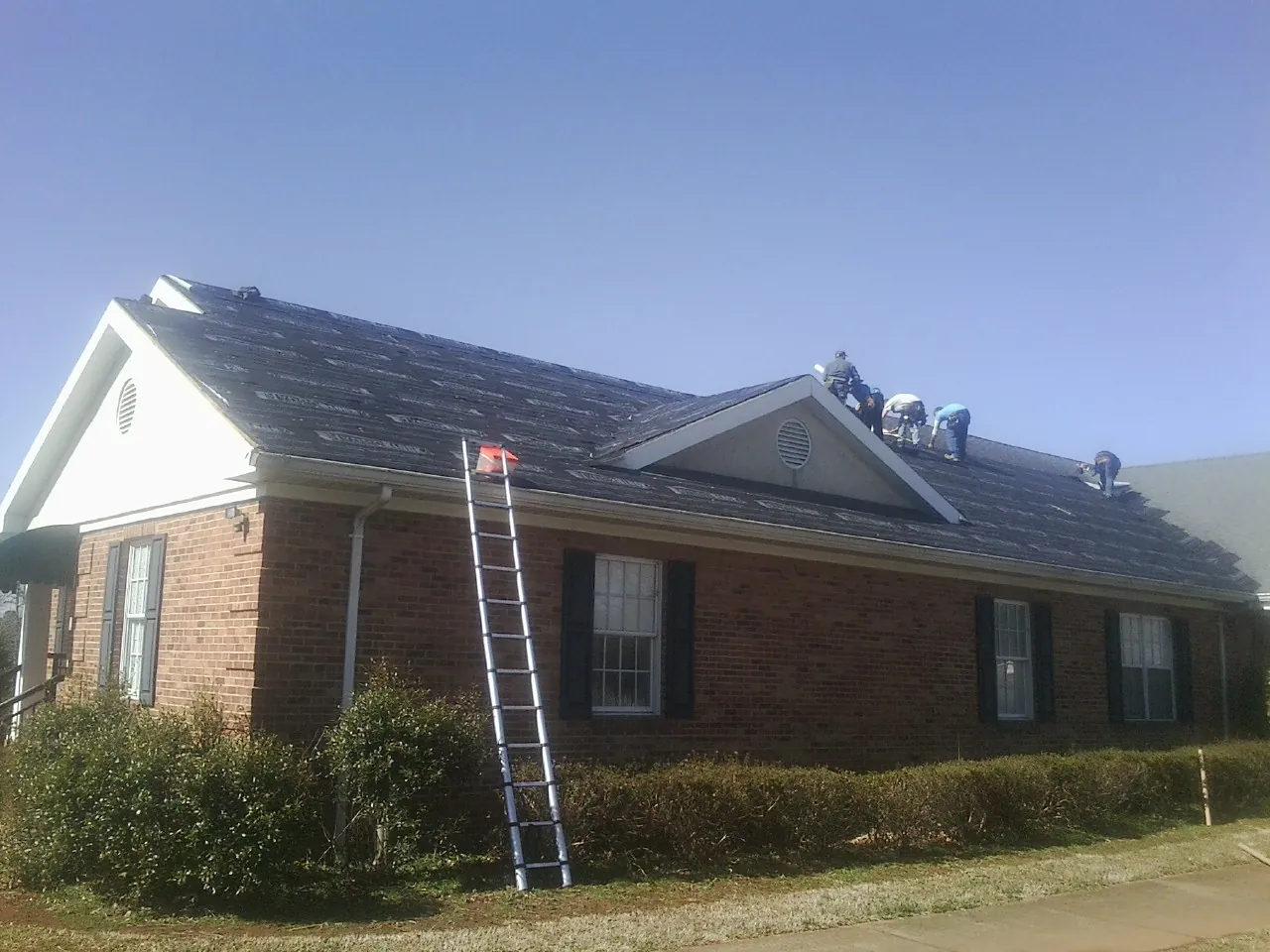 Crew tearing shingles off a brick ranch roof with a ladder set — Metal Roof Repair work by our crew in Great Mills