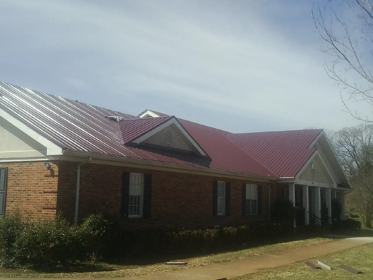 Red metal roof with gabled entries on a long brick building, from a Hail Damage Roof Repair job in Great Mills