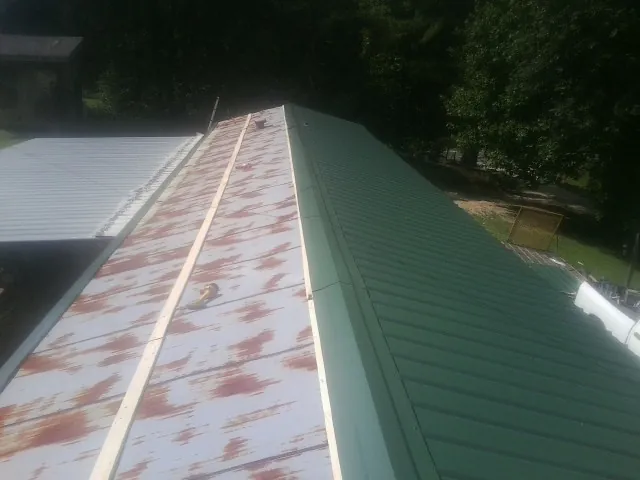 Old rusted panels beside newly installed green metal roofing — Wind Damage Roof Repair by Roofing Brothers in Great Mills