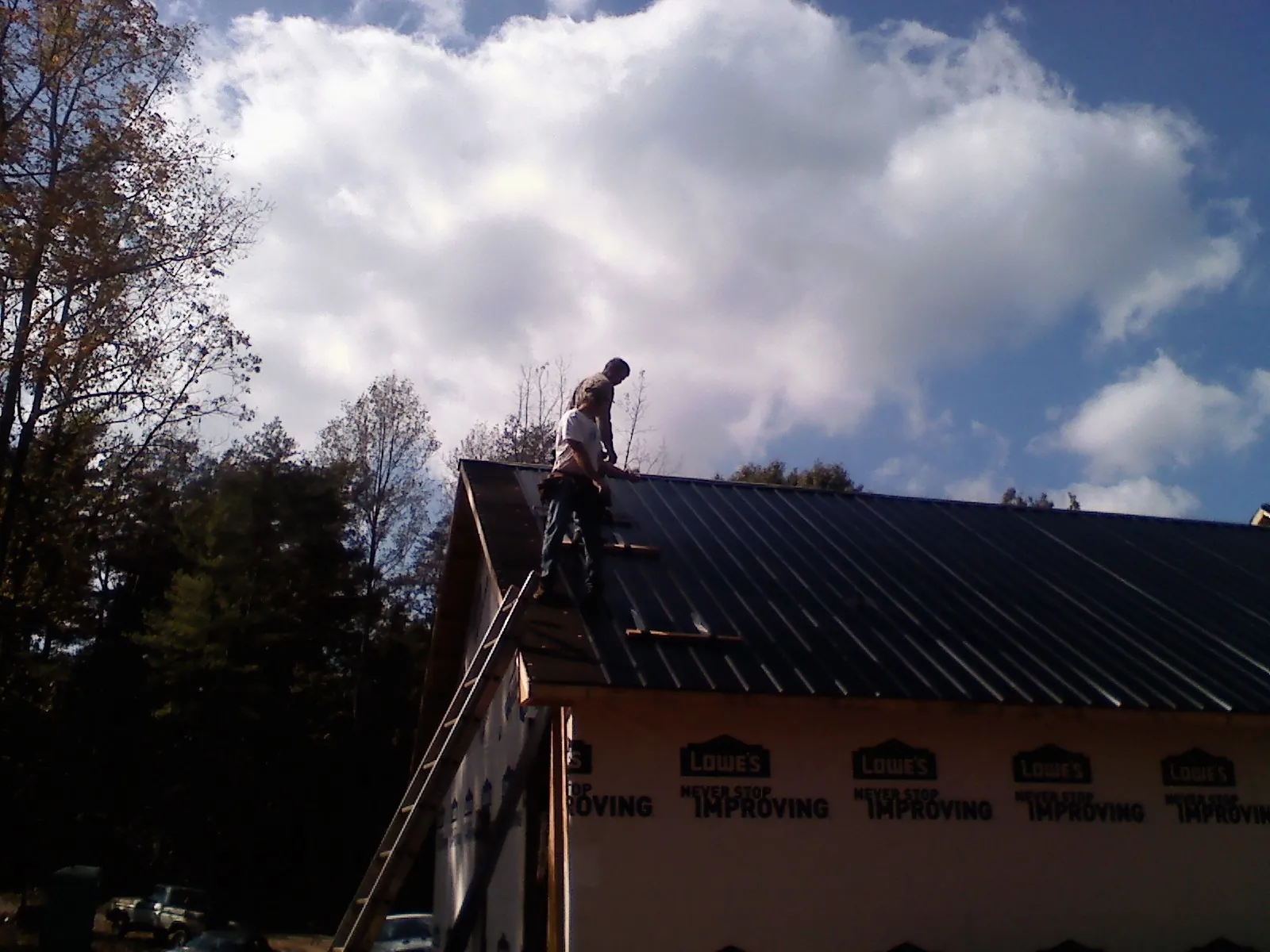 Roofer fastening dark metal panels high against a cloudy sky, from a Roof Inspection job in Great Mills
