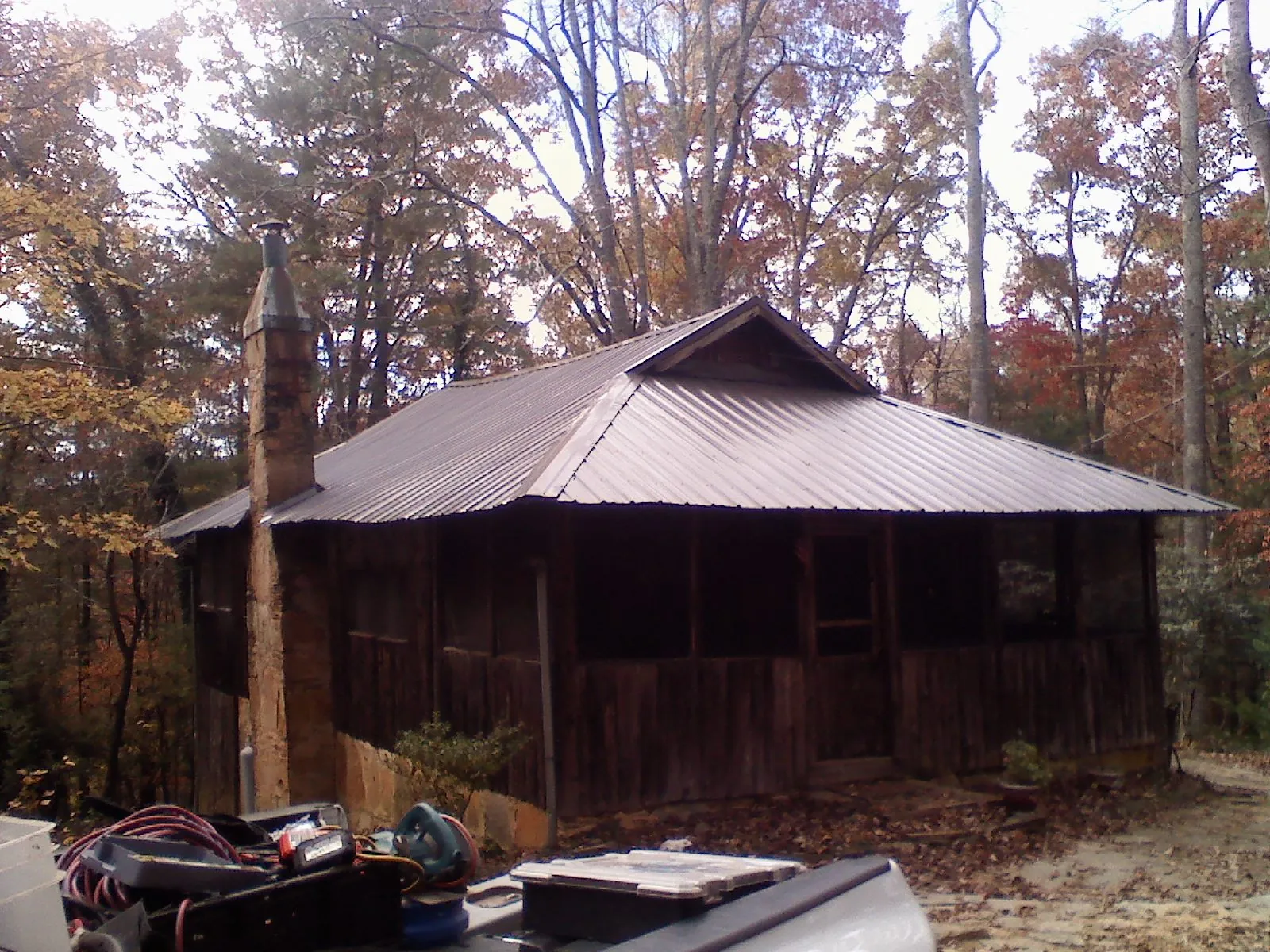 Brown metal hip roof on an old cabin with a stone chimney in Great Mills