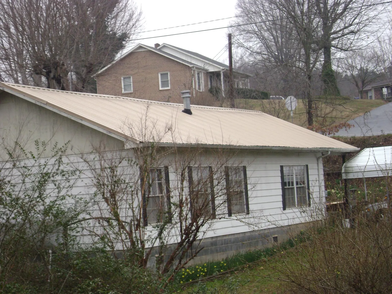 Tan metal roof on a white sided house set into a hillside — Commercial Roofing by Roofing Brothers in Great Mills